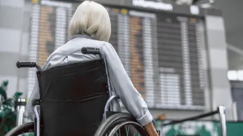 Blue badge holders should not pay airport drop-off fees, charity says Getty Images Wheelchair user photographed from behind looks at a large departures board in an airport
