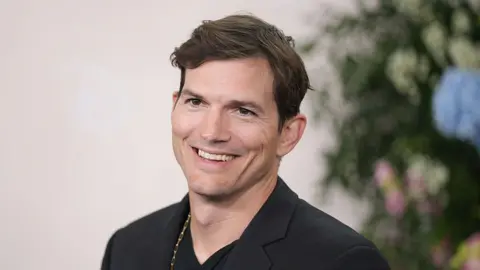 Soho House bought in £2bn deal as Ashton Kutcher joins board Getty Images A head and shoulders shot of Ashton Kutcher in which he looks at the camera and smiles. he has on a dark jacket and a gold chain around his neck.