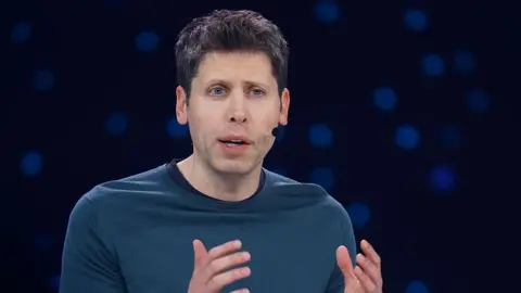 Getty Images Sam Altman hearing a headset microphone on stage at an event