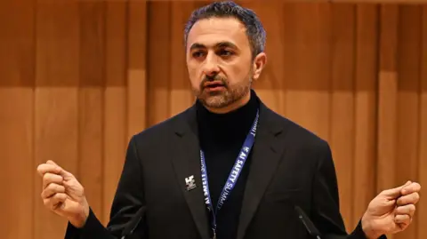 Microsoft boss troubled by rise in reports of 'AI psychosis' Getty Images Suleyman dressed all in black, with an AI safety summit lanyard round his next, addresses the audience.