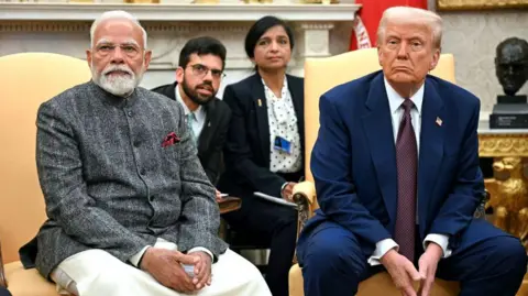 Inside the Indian factories hit hard by US's 50% tariffs Getty Images US President Donald Trump speaks with the press as he meets with Indian Prime Minister Narendra Modi in the Oval Office of the White House in Washington, DC. Both look at the camera with folded hands. Modi is wearing a traditional Indian kurta with a jacket, while Trump is in a navy blue suit and tie.