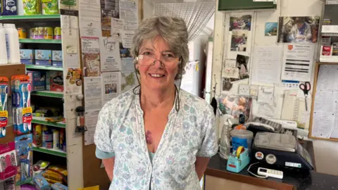 Sark shop to turn off freezers due to electricity price rise BBC A lady with grey short hair standing in a shop. there are toothbrushes, petfood and a till in the background.