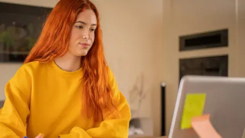 Tuition fees in England and Wales rise to £9,535 Getty Images A student with long red hair and a bright yellow jumper looks at her laptop screen.