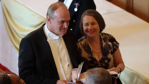 Ed Davey to boycott banquet over Gaza PA Media Liberal Democrat leader Sir Ed Davey walks alongside his wife Emily at the state banquet for Emmanuel Macron at Windsor Castle. He wears a formal black suit with white shirt and bow tie, while she wears a black and white floral dress with a pearl necklace.