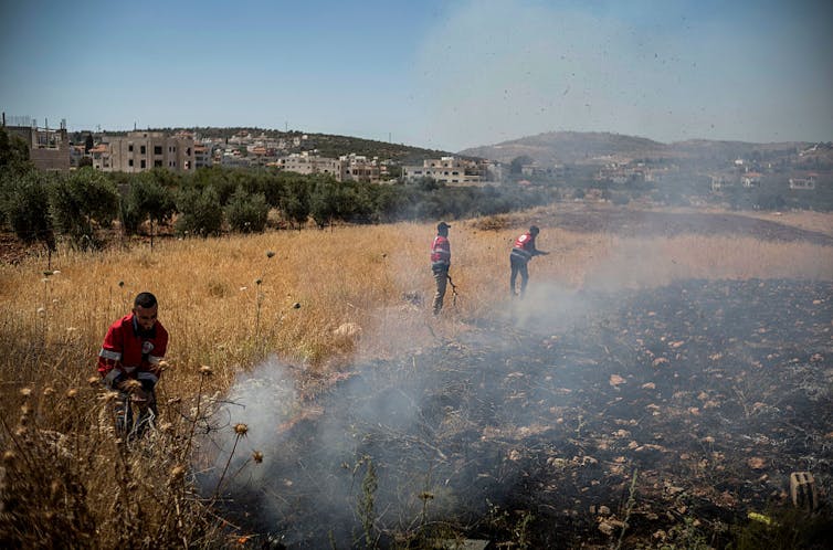 What’s fueling Israel’s surge of settler violence – and the lack of state response Three people walk through a field where the remains of a fire are smoldering.