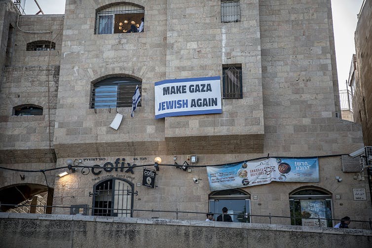 What’s fueling Israel’s surge of settler violence – and the lack of state response A blue-and-white sign hangs from a window on a three-story stone building.