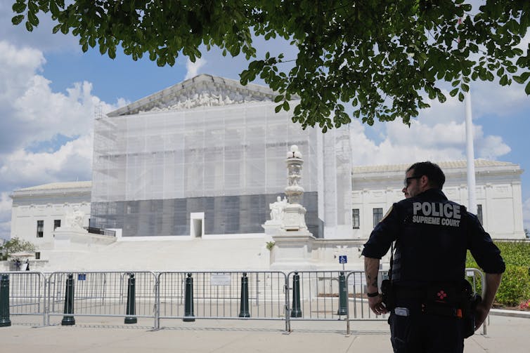 A police officer with his back to the camera stands outside the Supreme Court.