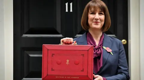 Budget to be held on 26 November, Rachel Reeves announces Getty Images Chancellor Rachel Reeves stands outside Number 11, Downing Street.
She is dressed in a navy blue suit with a remembrance poppy in her lapel and a plum coloured blouse, holds a red box containing the Autumn Budget in October 2024.