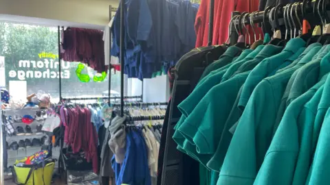 School costs a 'real struggle' for parents in Wales Racks of pre-loved school uniform and school shoes with green polo shirts in the foreground