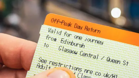 Peak time rail fares srapped on ScotRail trains Getty Images A close-up image of a train ticket from Edinburgh to Glasgow Central, held in someone's hand. The ticket is orange and white.