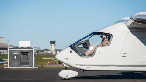Electric aviation awaits a battery breakthrough Beta Technologies Alia pulls up towards a charging station, the pilot is visible through the large cockpit window.