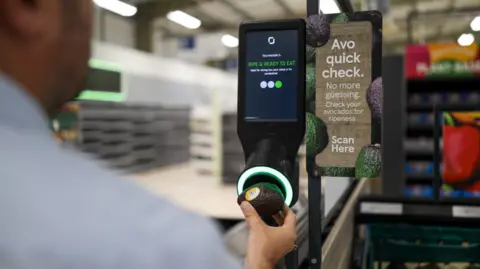 Tesco trials avocado ripeness scanners in five stores Tesco A man in a blue shirt holds an avocado to one of Tesco's new avocado scanners, the machine glows green and a screen reads 'ripe and ready to eat'
