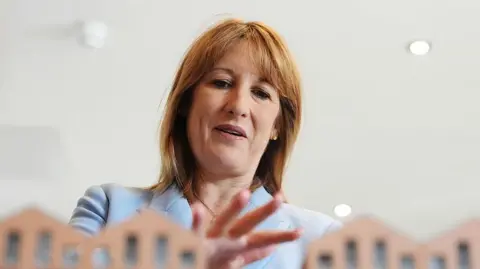 Market ructions and cabinet reshuffles will help shape Reeves' Budget WPA Pool/Getty Images Chancellor Rachel Reeves, wearing a powder blue suit, standing with her hand over some model houses which are just seen in front of her