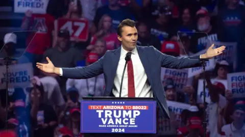 Report those who celebrate the shooting to employers, Vance says Getty Images An image of Charlie Kirk speaking at a Trump rally in Glendale, Arizona in August 2024. Behind him is a crowd donned in red, white and blue clothing, holding signs that say 'YOU'RE FIRED' and 'FIGHT! FIGHT! FIGHT!'. He is wearing a blue suit with a white button-up top and a red tie, speaking at a podium while gesturing widely with his hands. On the podium is a sign that reads 'TRUMP-VANCE MAKE AMERICA GREAT AGAIN 2024'.
