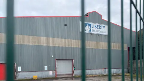 Rosyth shipyard expected to win £1bn Danish navy contract A grey warehouse building viewed through a green wire fence. A sign on the building reads Liberty Steel Dalzell