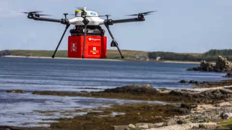 Will drones deliver your next hot food order? Skyports/Royal Mail A white Skyports drones carries a red box with the Royal Mail logo, over a beach with the sea in the background.