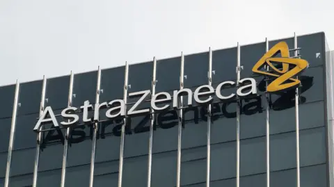 AstraZeneca pauses £200m Cambridge investment Getty Images Pharmaceutical company Astrazeneca's logo on the side of an office building with dark opaque windows. There is a grey sky behind the building.