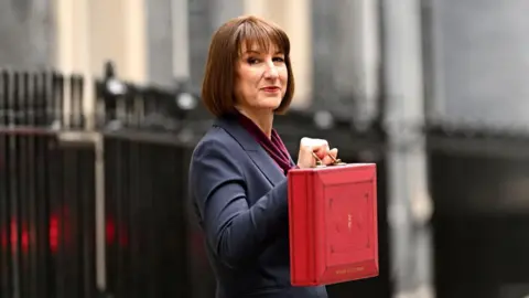 Market ructions and cabinet reshuffles will help shape Reeves' Budget Leon Neal/Getty Images Chancellor Rachel Reeves, wearing a dark blue suit, holding the red Budget box, standing in front of the black railings on Downing Street, looking to the side and straight into the camera