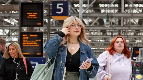 Scotland scrapped peak rail fares Getty Images Members of the public make their way through Central Station in Glasgow, Scotland, including a woman with blonde hair, a denim jacket and glasses.