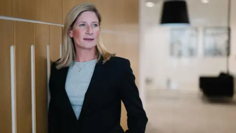 MoJ owes us £20m after contractor ISG's collapse, say suppliers Hill Dickinson Sarah Emerson is a corporate photo. She has blonde hair and is wearing a slick black suit with a grey top and a necklace. We can see she is an office somewhere but the background is blurred.