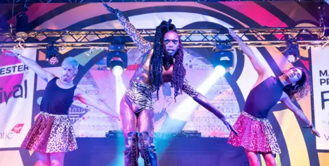 Manchester Pride goes bust with thousands owed in unpaid fees Getty Images Artist Black Peppa performs during Manchester Pride 2022 - they're pictured mid-dance with their arms outstretched while wearing leopard and zebra print spandex alongside two performers wearing leotards.