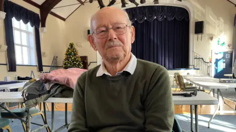 Norfolk council roadshow aims to help people with household bills Clare Worden/BBC Richard Carter wears glasses and an olive sweatshirt. He has a grey moustache.