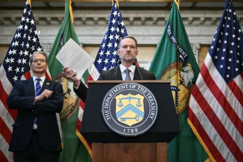 Bankers on edge, a gilded cash room and US blaming China Getty Images A suited Scott Bessent is stood behind Jamieson Greer who is at a podium facing the camera clutching papers and with USA flags behind him