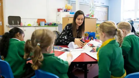 Families are priced out of London, Assembly told Getty Images A primary school teacher sitting with a group of young children in green school jumpers at a table in a classroom.