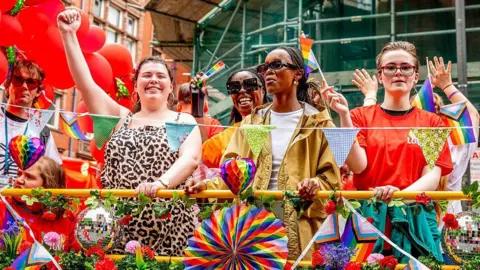 The fall and future of Manchester Pride Getty Images Five people pictured behind a barrier at Manchester Pride. They are waving pride flags smiling and waving. The barrier is decorated with various rainbow flags and disco balls.