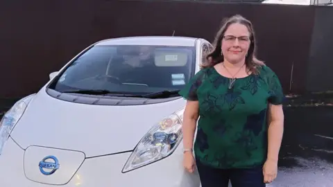 How to tell the health of a battery in a used EV Lucy Crawford Wearing a dark green top, Lucy Crawford stands next to her white Nissan Leaf