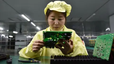 China's economic growth slows as trade tensions with US flare up Getty Images A women in a yellow attire holds a green circuit board in a production facility in East China