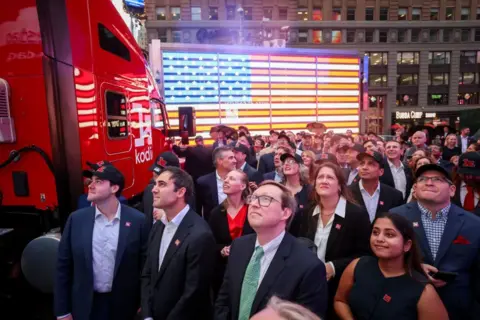 Bankers on edge, a gilded cash room and US blaming China Getty Images People dressed in suits are in Times Square looking upwards off camera next to a red truck that says Kodiak AI on its side.