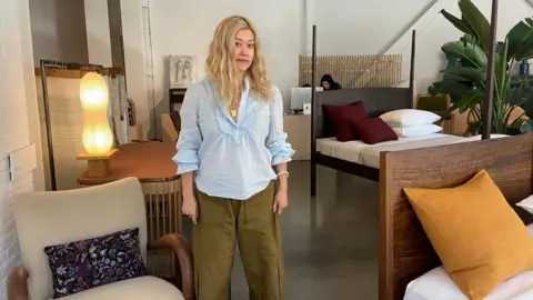 New Trump tariffs pose another hurdle for the housing market Danielle Kaye Jean Lin, the founder of a design gallery for furniture and home decor called Colony, stands in her store in lower Manhattan wearing a blue shift and looking at the camera while surrounded by beds, chairs, tables and lamps.