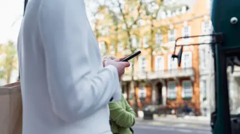 Tech bosses could stop mobile phone theft, say MPs Getty Images Woman in white cardigan looks at mobile phone in a London street