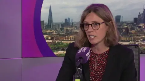 'You're willing to lose money, but not the person' A woman with mid-length blonde hair sat at a microphone in the BBC London studio. She is wearing a black jacket and glasses, with a screen displaying the London skyline behind her.