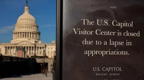 As US shutdown starts to bite, how much could it hit economy? Getty Images The Capitol in the background with a black sign saying the U.S. Capitol Visitors Center is closed to due to a lapse in appropriations in the foreground.