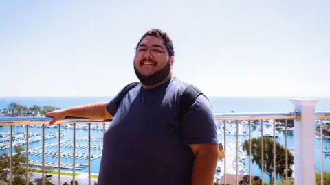 New Trump tariffs pose another hurdle for the housing market Anthony Cabrera Anthony Cabrera poses for a photo in front of a body of water, wearing a t-shirt and glasses and carrying a backpack.