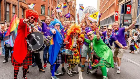The fall and future of Manchester Pride Getty Images Manchester Pride parade. People dressed in brightly-coloured suits holding pride flags. Some are holding large drums and colourful kilts. They are posing with their arms held out and smiling in the street.