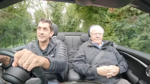 Reed says 'job on the line' over 1.5m housing target as experts warn meeting it unlikely BBC climate editor Justin Rowlatt, dressed in black puffer coat, drives an open-top car down a country lane, beside economist Paul Cheshire in the passenger seat, whose hands are folded across his stomach