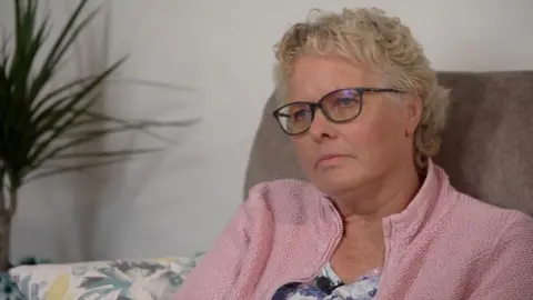 Thousands sue company alleging it hid talcum powder cancer risks Siobhan has short pale blonde hair, black glasses and a pink jacket and sits in a brown chair in front of a potted plant.