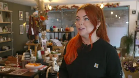 Spooky spending creeping in weeks before Halloween BBC Charlotte Brennan with long, bright orange hair and a black sweater stands in front of her gift shop items which includes homeware,ghost-shaped pillows, dried flowers, candles and ornaments