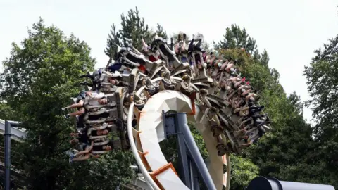 Our biggest competition is screens at home, says theme park boss Getty Images The Nemesis rollercoaster - showing a section of its track where a carriage of riders are in the middle of a rotation, with some riders off to the side of the ride, and some upside down - some trees are visible in the background