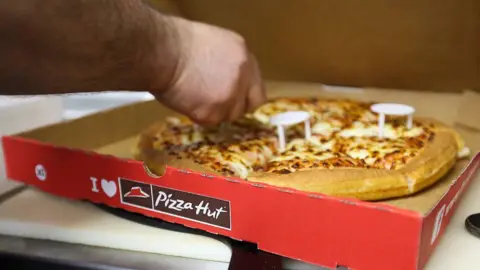 Pizza Hut to close 68 UK restaurants after falling into administration Getty Images A person reaches into a pizza box and cuts a pizza