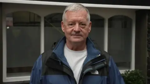 All Post Office Horizon victims entitled to free legal advice for first time Tony Downey Tony Downey, a white man, wearing a black and blue rain coat over a grey t shirt.