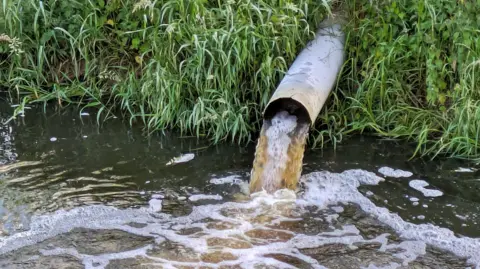 Fining firms for sewage spills will get 'quicker and easier', says government Getty Images An overflow pipe discharges a brown liquid into a stream or river.