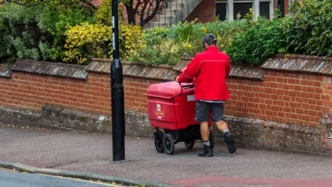 Royal Mail fined £21m by Ofcom for missing delivery targets Getty Images A postman pushes a red Royal Mail cart down a residential street