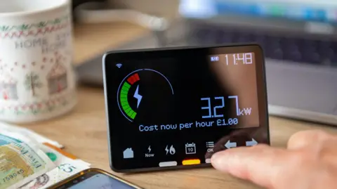Energy standing charge plans could backfire, MPs told Getty Images A smart meter display on a table with a mug, £5 notes and a smartphone alongside it.