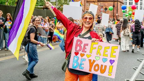 Manchester Pride goes bust with thousands owed in unpaid fees Getty Images A photograph of part of Manchester Pride's parade in 2025. Someone is holding a colourful banner which says 'be free, be you' on it. They are wearing brightly coloured clothing including a red jacket, orange trousers and tinted sunglasses. They are waving a flag in their other hand. Crowds are gathered on a pavement and on the street behind them.