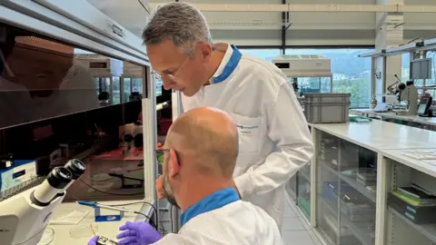 Swiss companies target alternative export markets MPS In a white lab coat, Gilles Robert speaks to a colleague who is holding an electrical device.