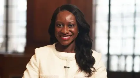 Bank of England chief Afua Kyei tops 2026 Powerlist as UK's most influential black person BBC Afua Kyei wears a white suit jacket with a beaded trim. She has long dark hair and is smiling.